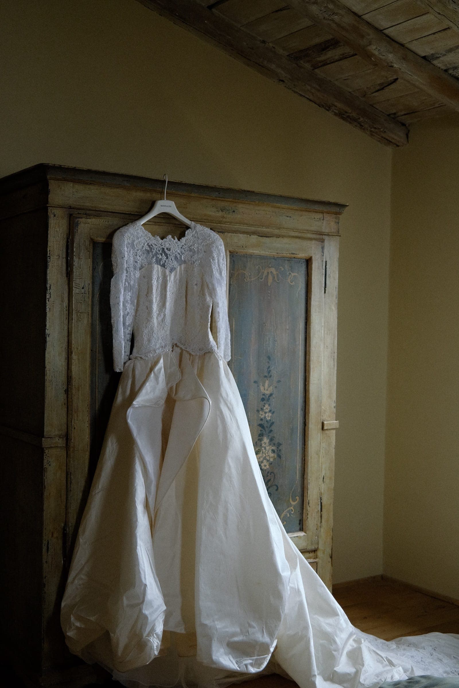 Abito da sposa di pizzo ereditato appeso a un armadio antico dipinto